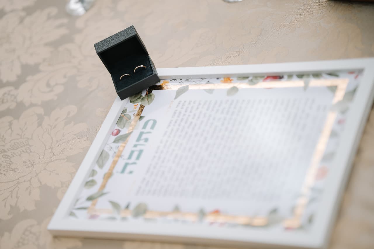 Framed ketubah on table with wedding rings in a box