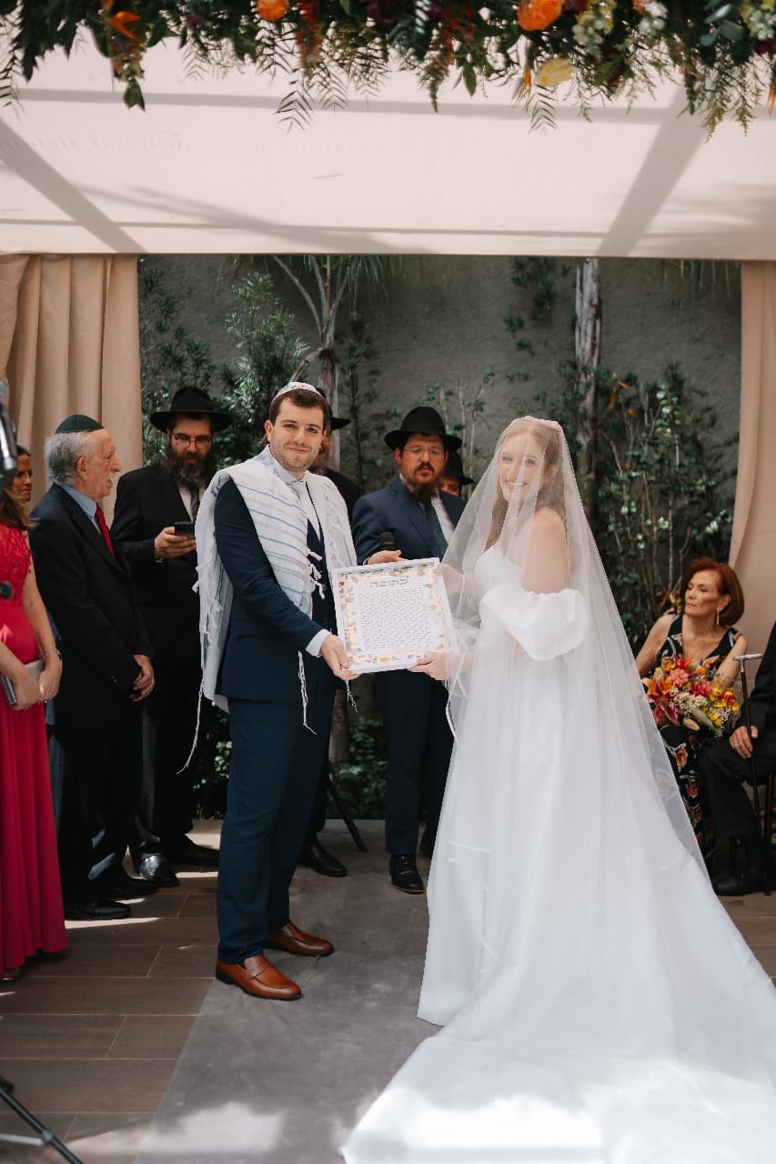 Couple holding ketubah under the chuppah at outdoor ceremony